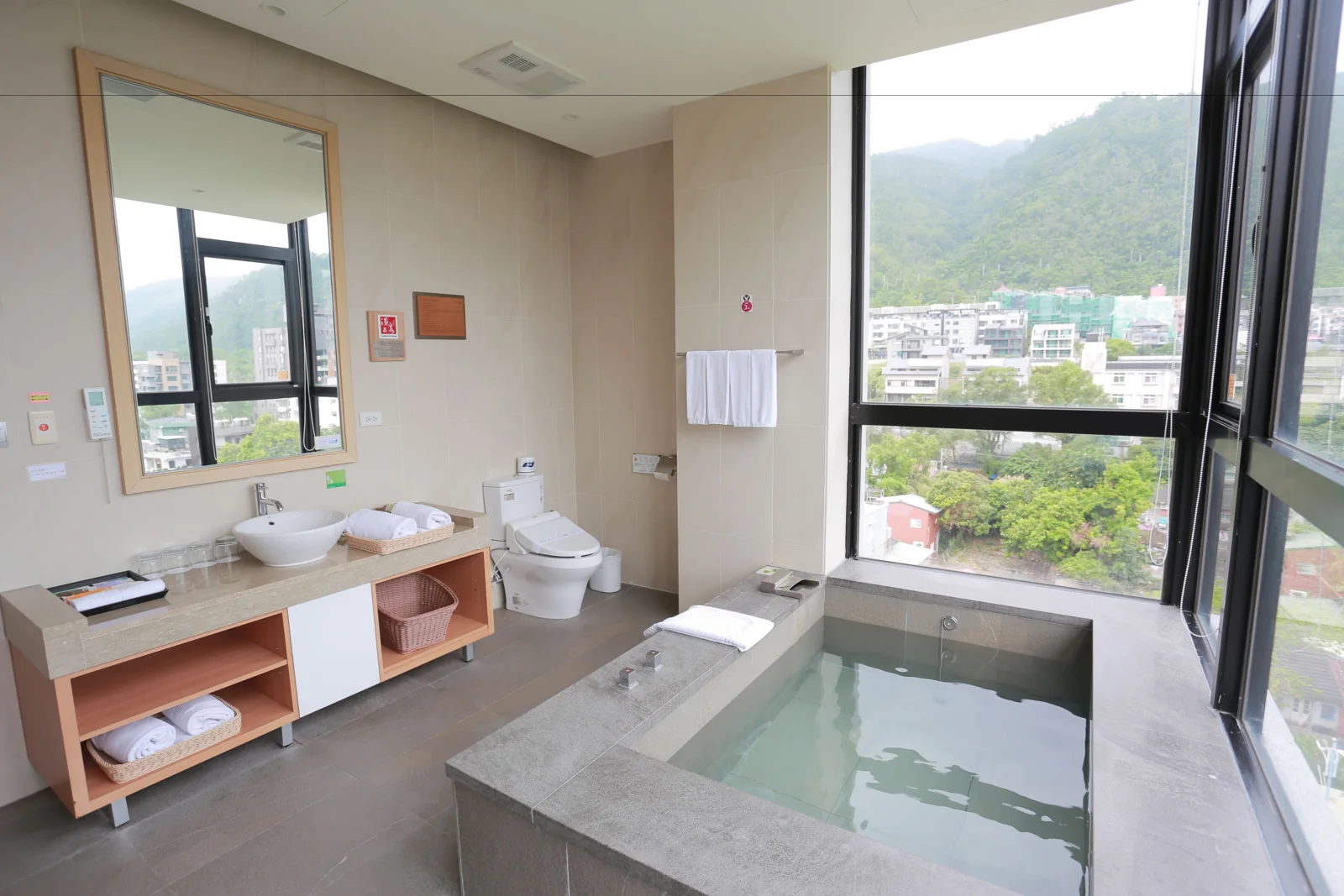 佧美特定浴室的方形石材池、大面窗戶與窗外山坡市街